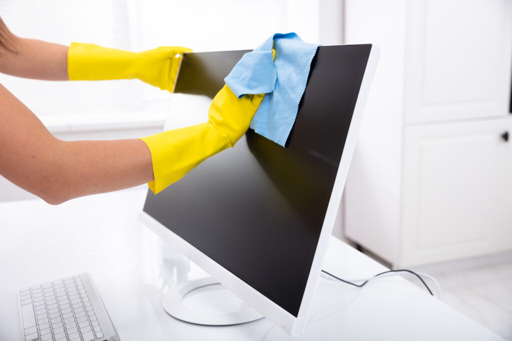 A person is wearing gloves and using a microfiber cloth to wipe down a computer monitor